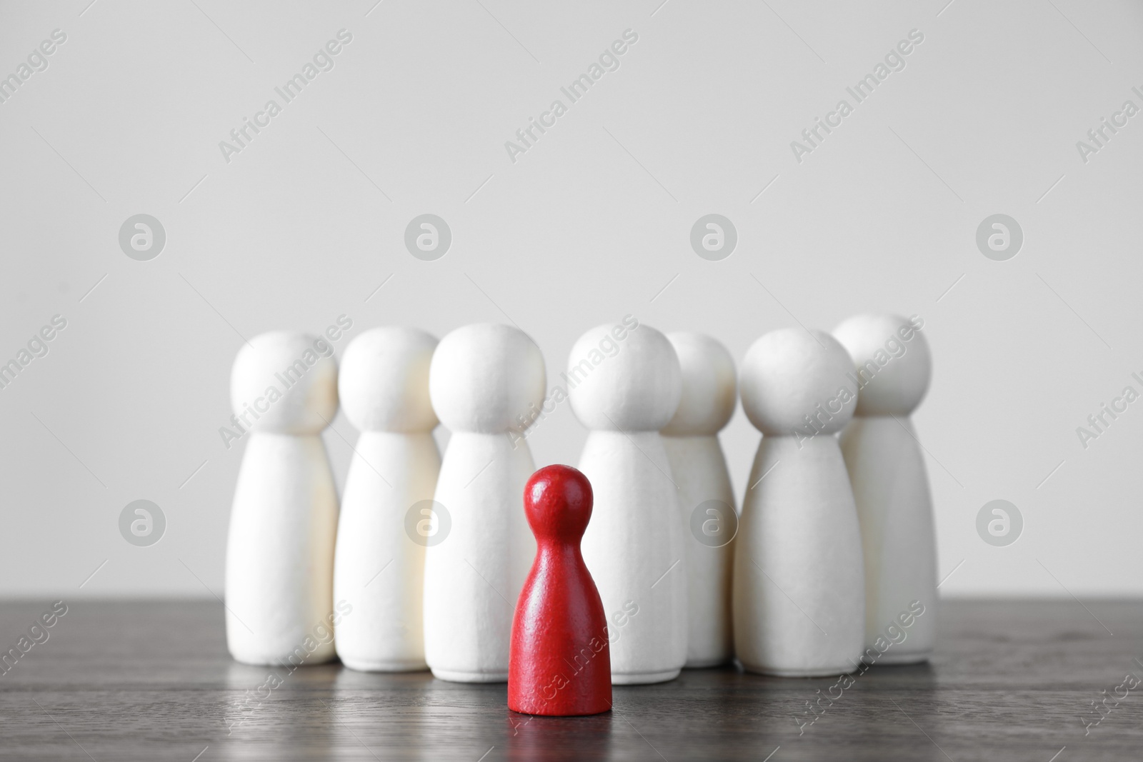 Photo of Human resources concept. Red figure among wooden ones on table against light background, closeup. Space for text