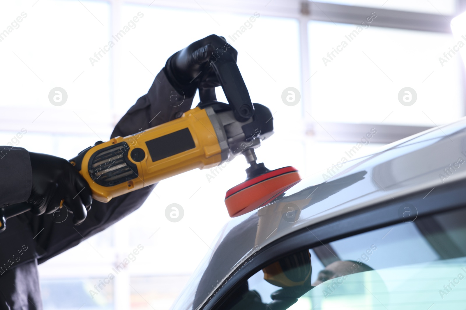 Photo of Man polishing car with orbital polisher indoors, closeup