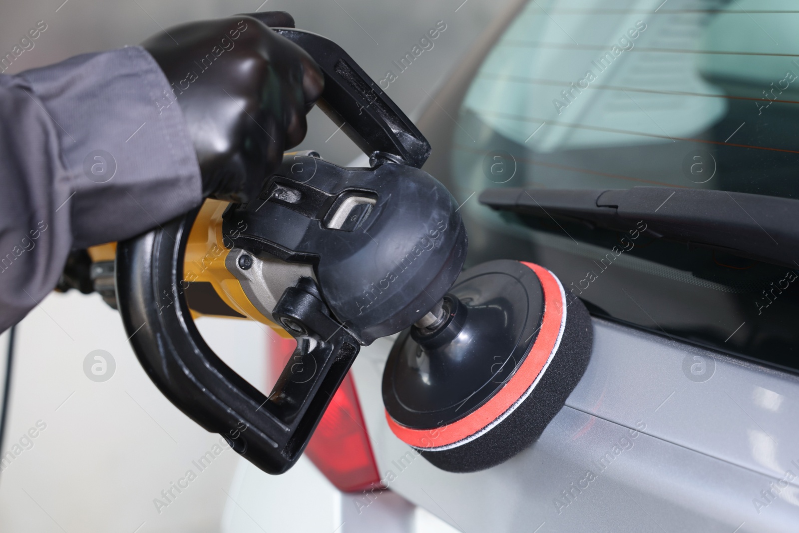 Photo of Man polishing car with orbital polisher indoors, closeup