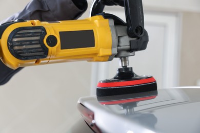 Photo of Man polishing car with orbital polisher indoors, closeup