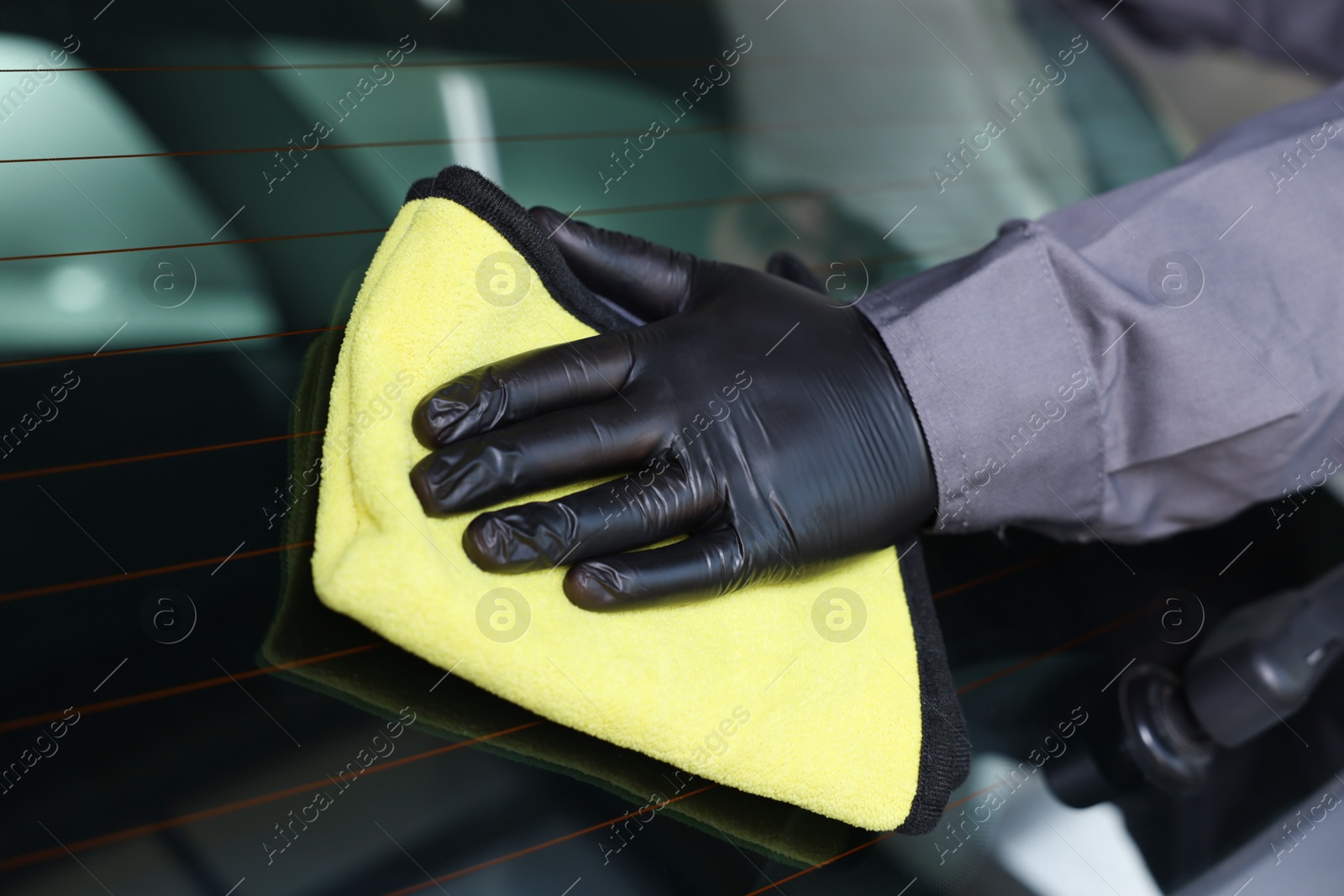 Photo of Man polishing car rear window with yellow rag indoors, closeup