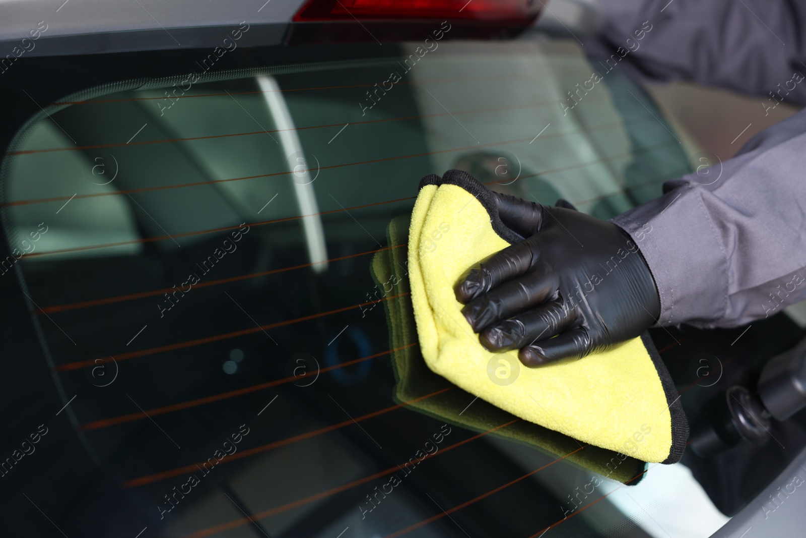 Photo of Man polishing car rear window with yellow rag indoors, closeup