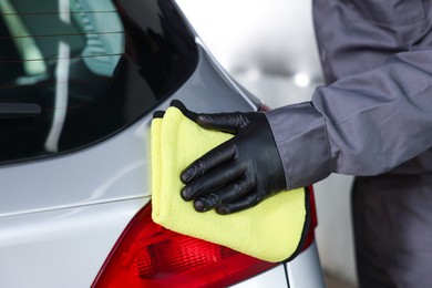 Photo of Man polishing car rear light with yellow rag indoors, closeup