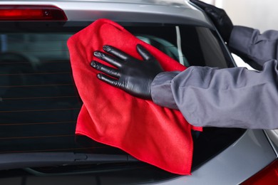 Photo of Man polishing car rear window with red rag indoors, closeup