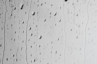 Water drops on light grey glass surface, closeup