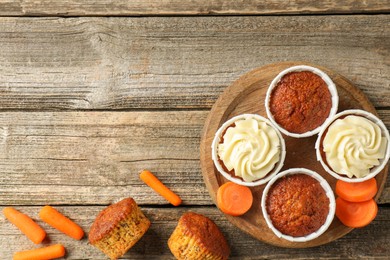 Photo of Delicious carrot muffins and fresh vegetables on wooden table, flat lay. Space for text