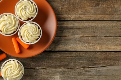 Photo of Delicious carrot muffins and fresh vegetables on wooden table, flat lay. Space for text