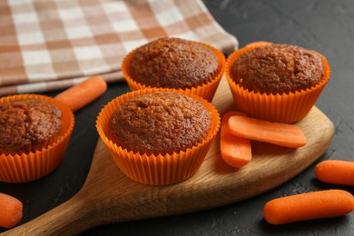 Photo of Delicious carrot muffins with fresh vegetables on black table, closeup