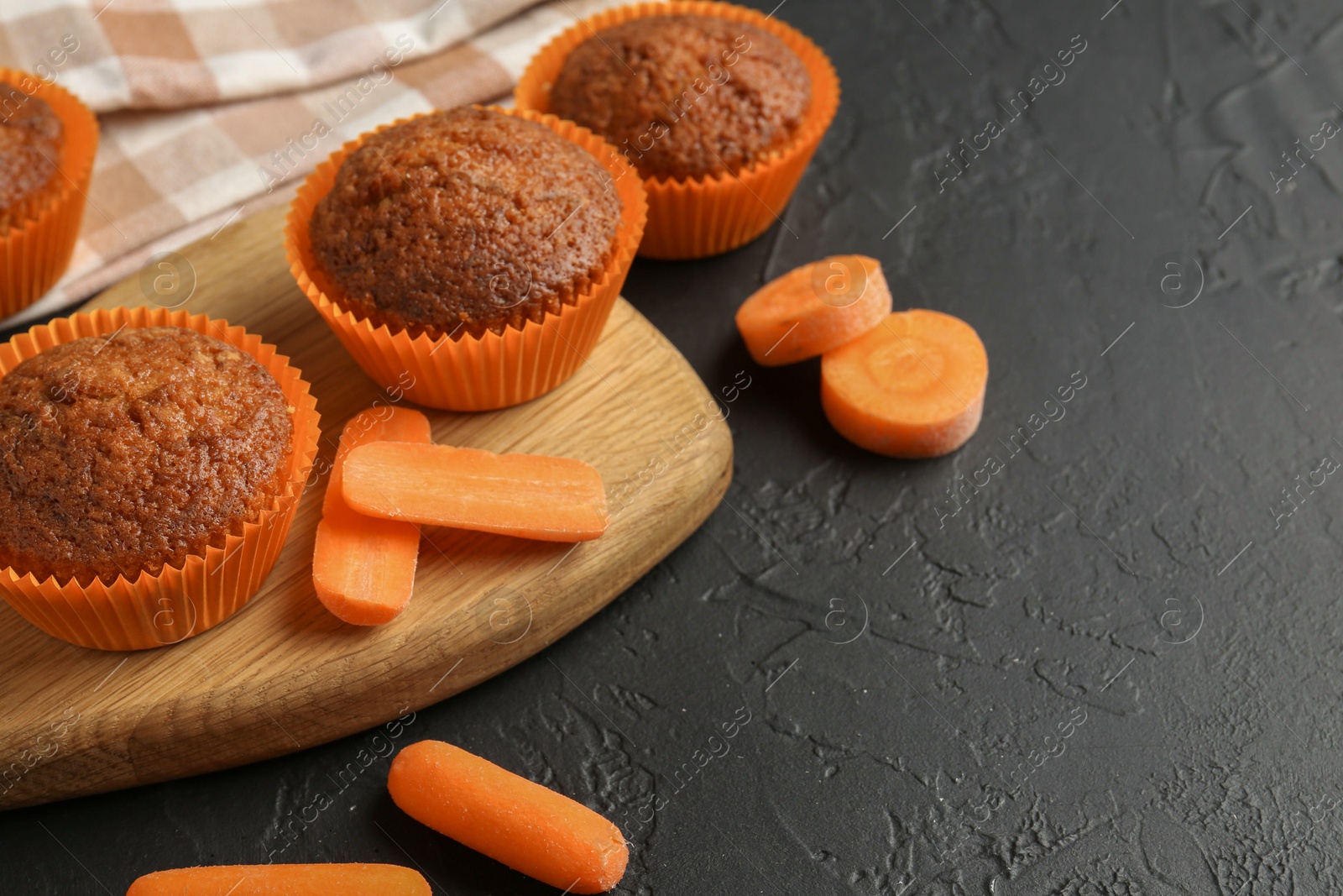 Photo of Tasty carrot muffins with fresh vegetables on black table, closeup. Space for text