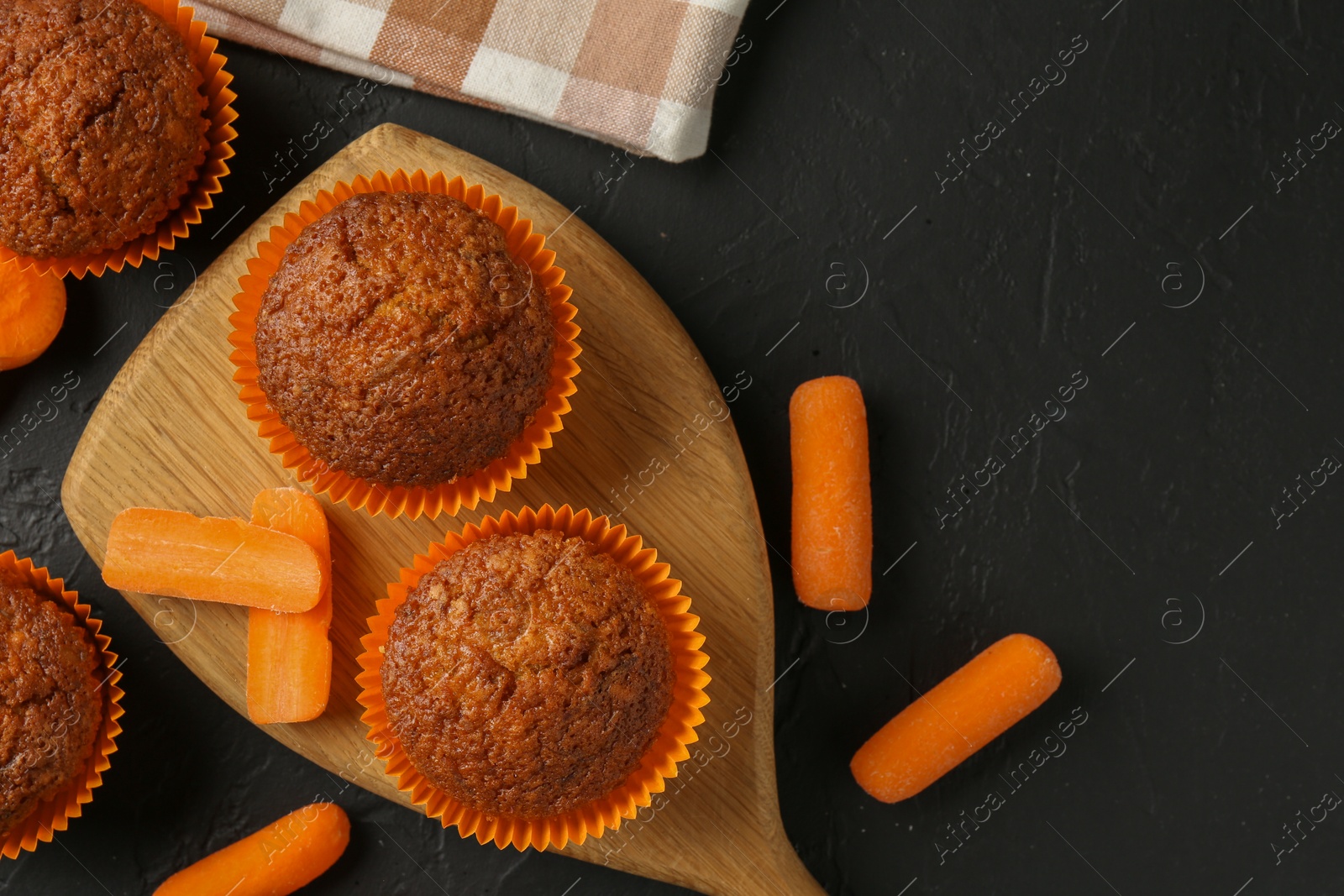 Photo of Delicious carrot muffins with fresh vegetables on black table, flat lay. Space for text