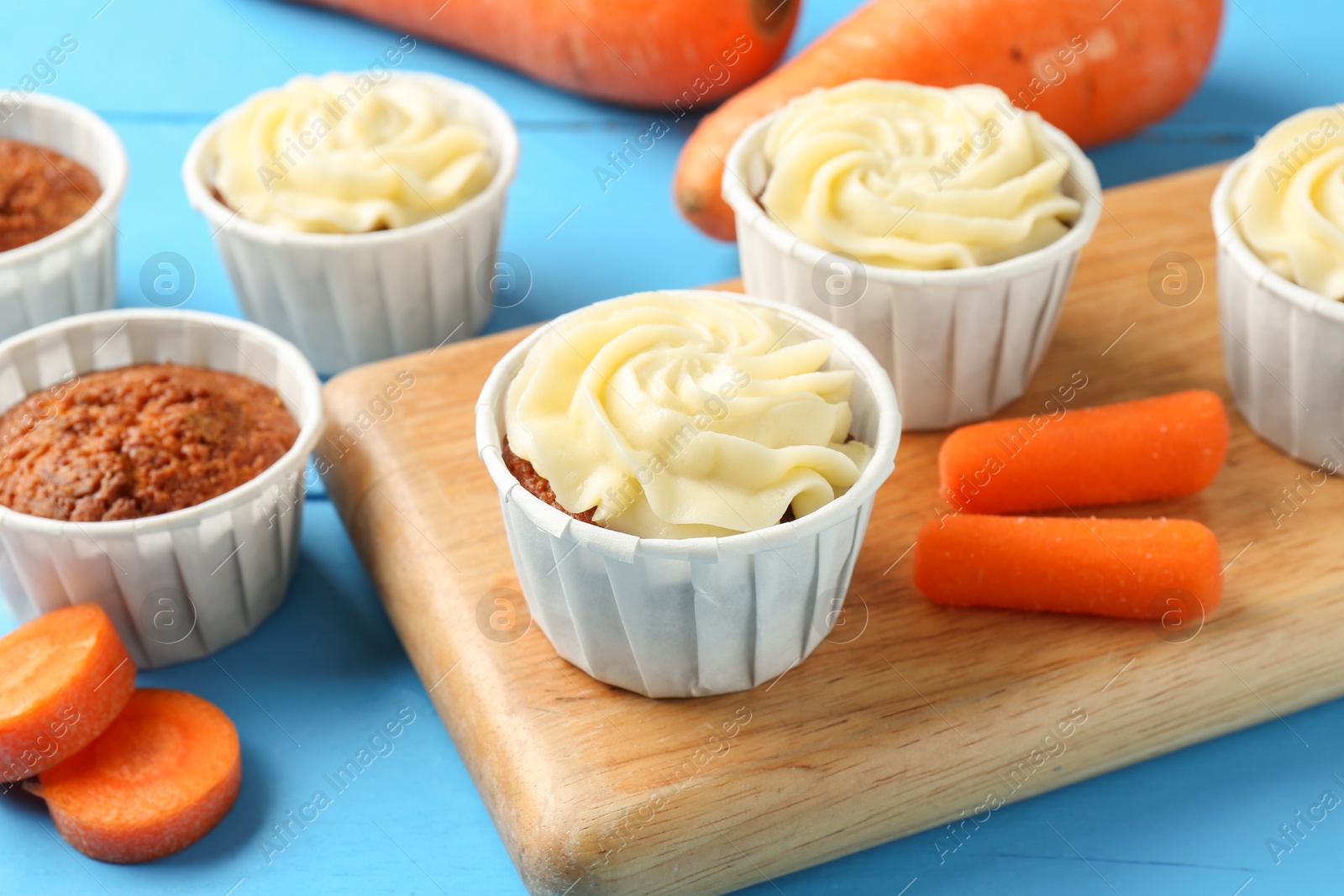 Photo of Tasty carrot muffins with fresh vegetables on light blue wooden table, closeup