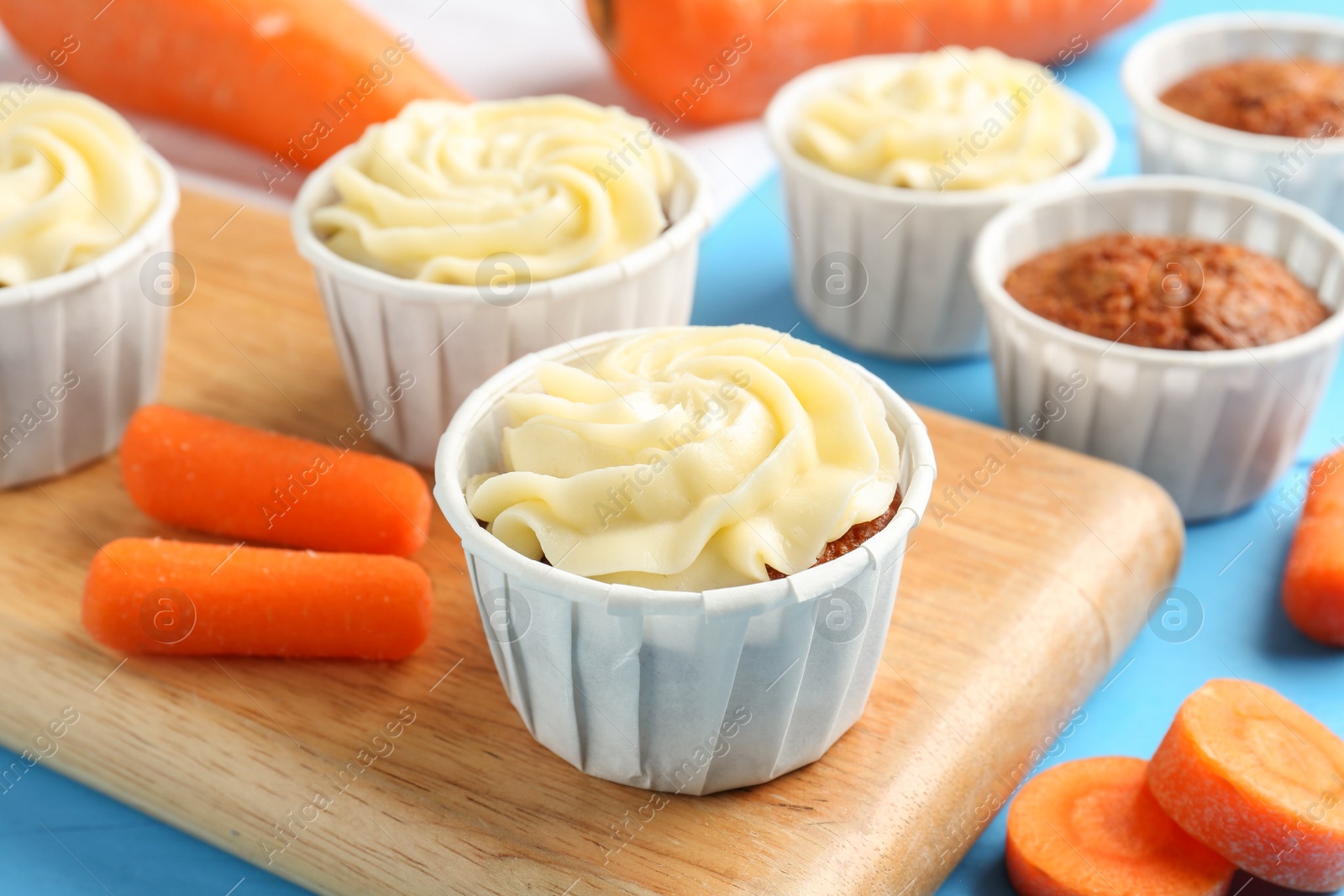 Photo of Tasty carrot muffins with fresh vegetables on light blue table, closeup