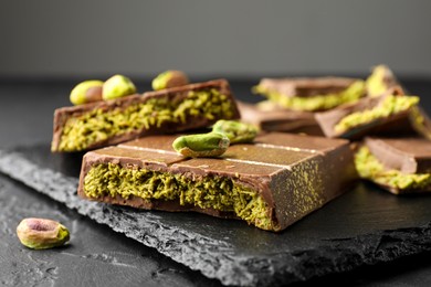 Photo of Pieces of Dubai chocolate bar with pistachios and knafeh on grey table, closeup