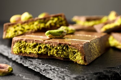 Photo of Pieces of Dubai chocolate bar with pistachios and knafeh on grey table, closeup