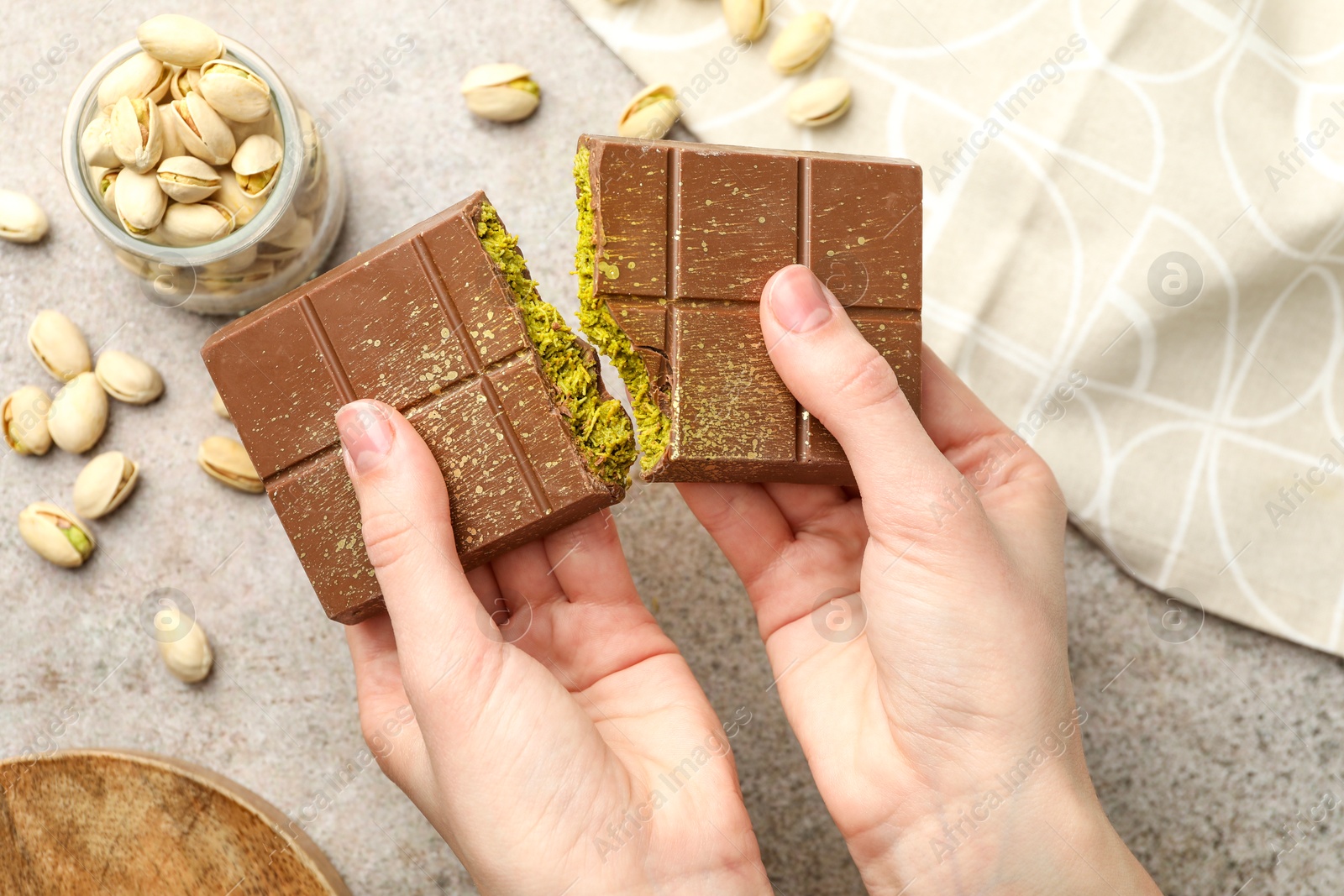 Photo of Woman breaking Dubai chocolate bar with pistachios and knafeh at grey table, closeup