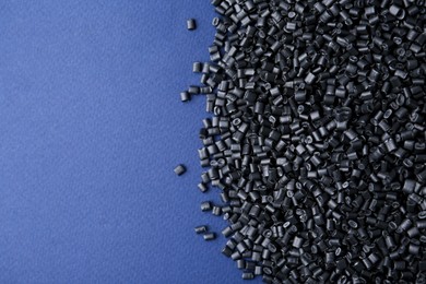 Photo of Pile of black plastic granules on blue background, top view. Space for text