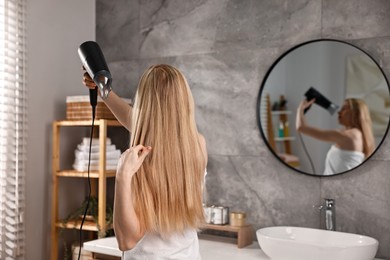 Photo of Beautiful young woman drying her hair in bathroom, back view