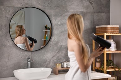 Photo of Beautiful young woman drying her hair in bathroom