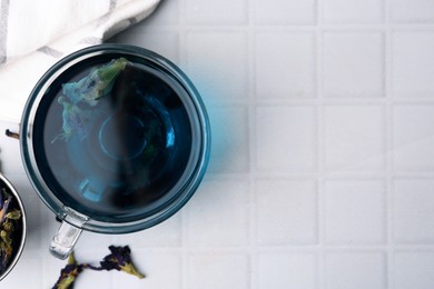 Photo of Delicious butterfly pea flower tea on white tiled table, flat lay. Space for text