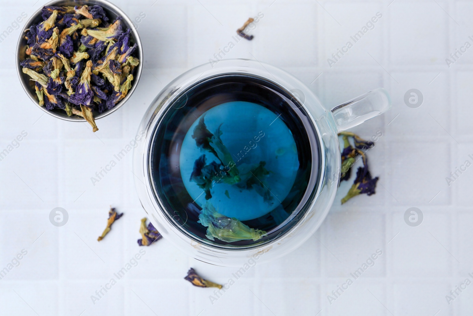 Photo of Delicious butterfly pea flower tea on white tiled table, flat lay