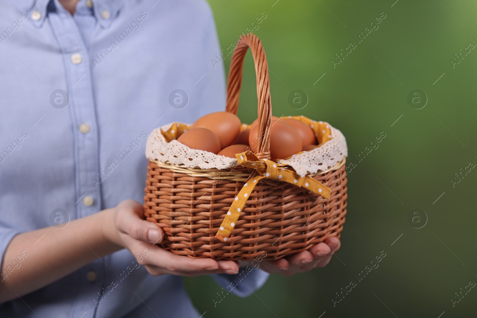 Photo of Woman with basket of raw eggs on blurred background, closeup