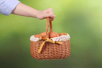 Photo of Woman with basket of raw eggs on blurred background, closeup