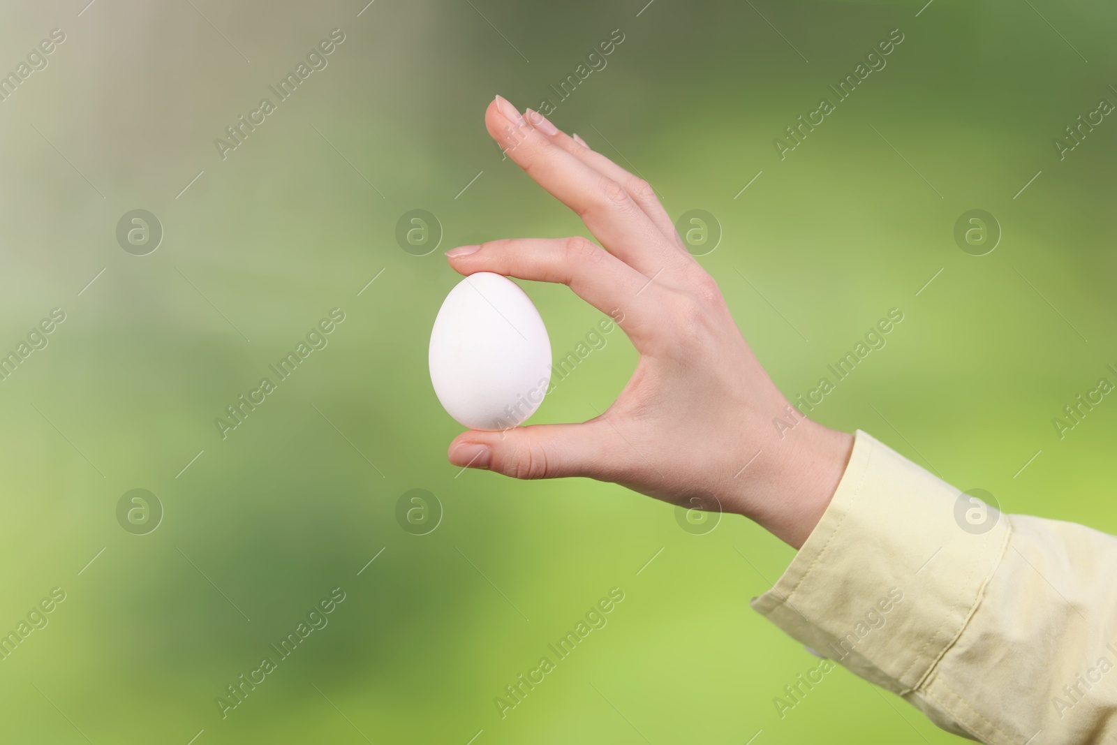 Photo of Woman holding raw egg on blurred background, closeup