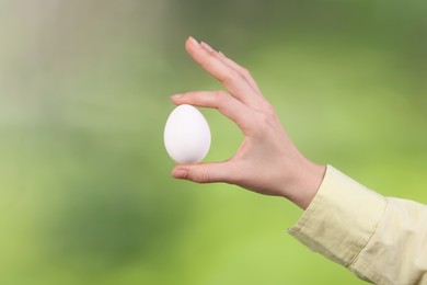 Photo of Woman holding raw egg on blurred background, closeup