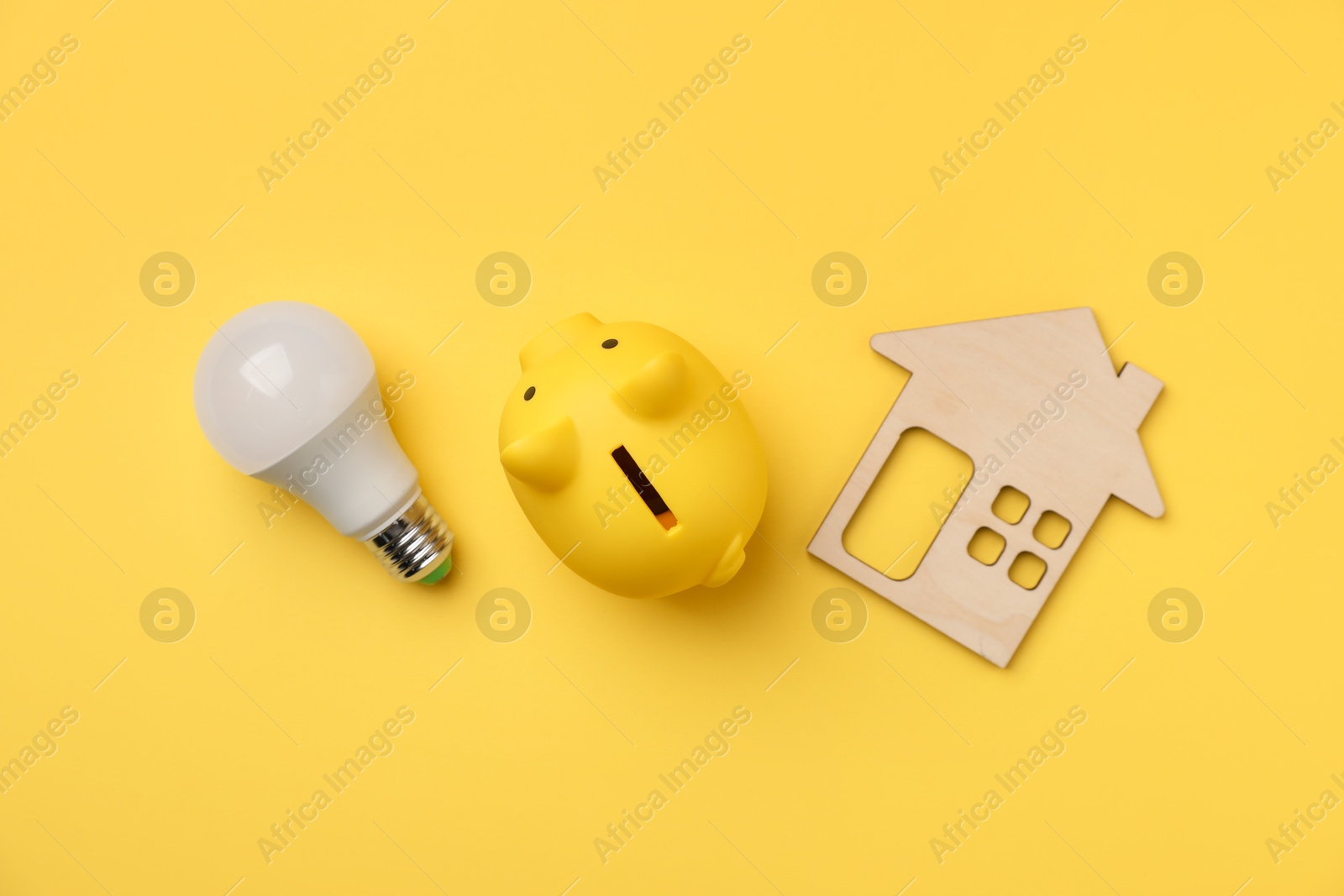 Photo of Piggy bank, light bulb and house model on yellow background, flat lay. Energy saving concept