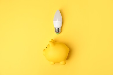 Photo of Light bulb and piggy bank on yellow background, flat lay. Energy saving concept