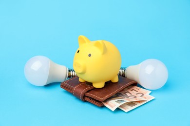 Photo of Piggy bank, lightbulbs and purse with euro banknotes on light blue background. Energy saving concept