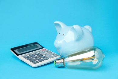 Photo of Piggy bank, calculator and lightbulb on light blue background. Energy saving concept