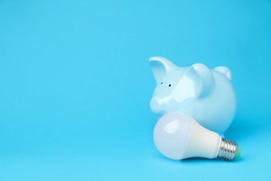 Photo of Piggy bank and lightbulb on light blue background, space for text. Energy saving concept