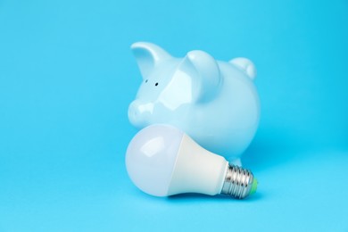 Photo of Piggy bank and lightbulb on light blue background, closeup. Energy saving concept