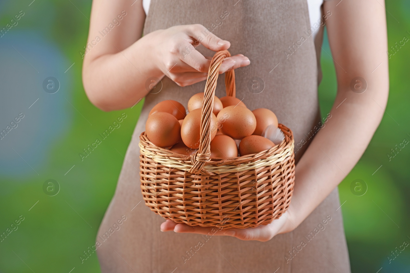 Photo of Woman with basket of eggs on blurred background, closeup