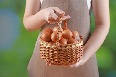 Photo of Woman with basket of eggs on blurred background, closeup