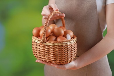 Photo of Woman with basket of eggs on blurred background, closeup