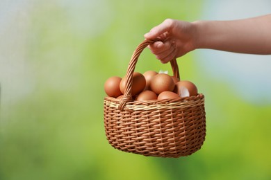 Photo of Woman with basket of eggs on blurred background, closeup. Space for text