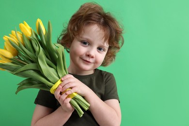 Photo of Cute little boy with bouquet of tulips on green background. Space for text