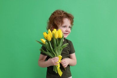 Cute little boy with bouquet of tulips on green background