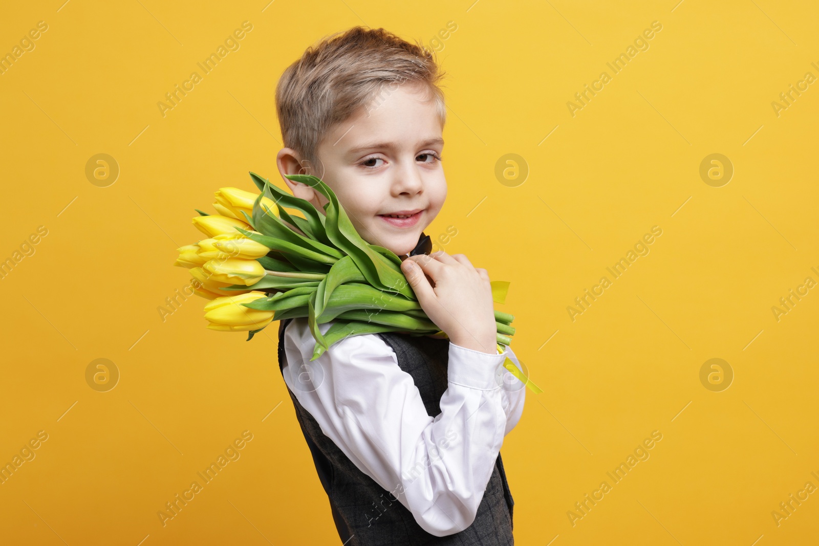 Photo of Cute little boy with bouquet of tulips on yellow background. Space for text