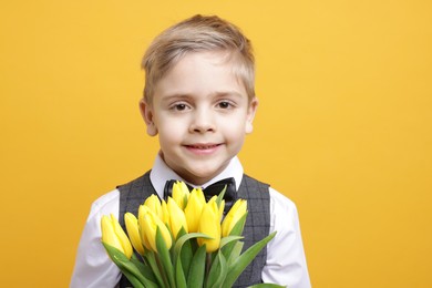 Cute little boy with bouquet of tulips on yellow background