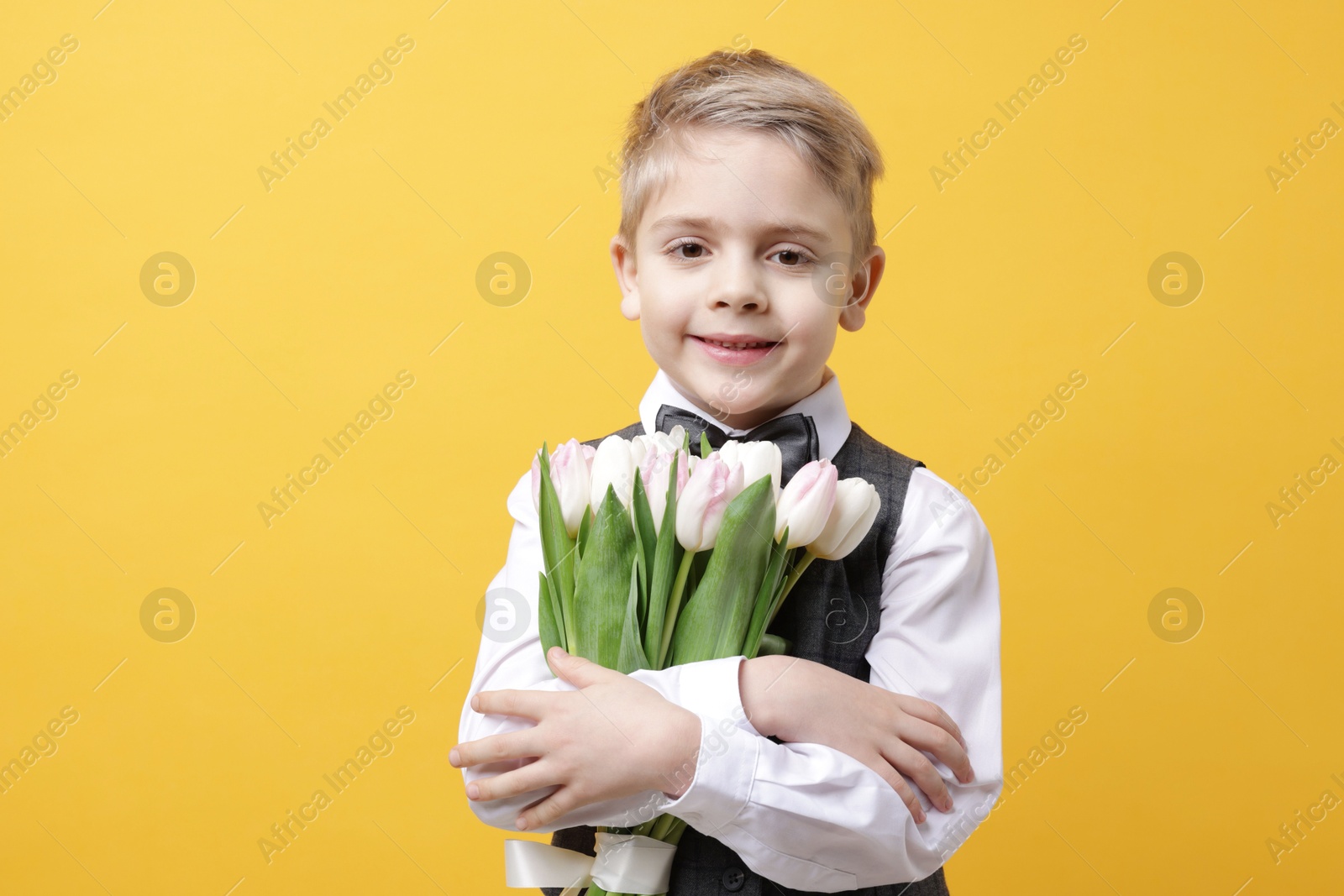 Photo of Cute little boy with bouquet of tulips on yellow background