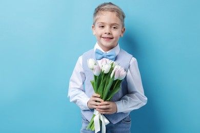 Photo of Cute little boy with bouquet of tulips on light blue background