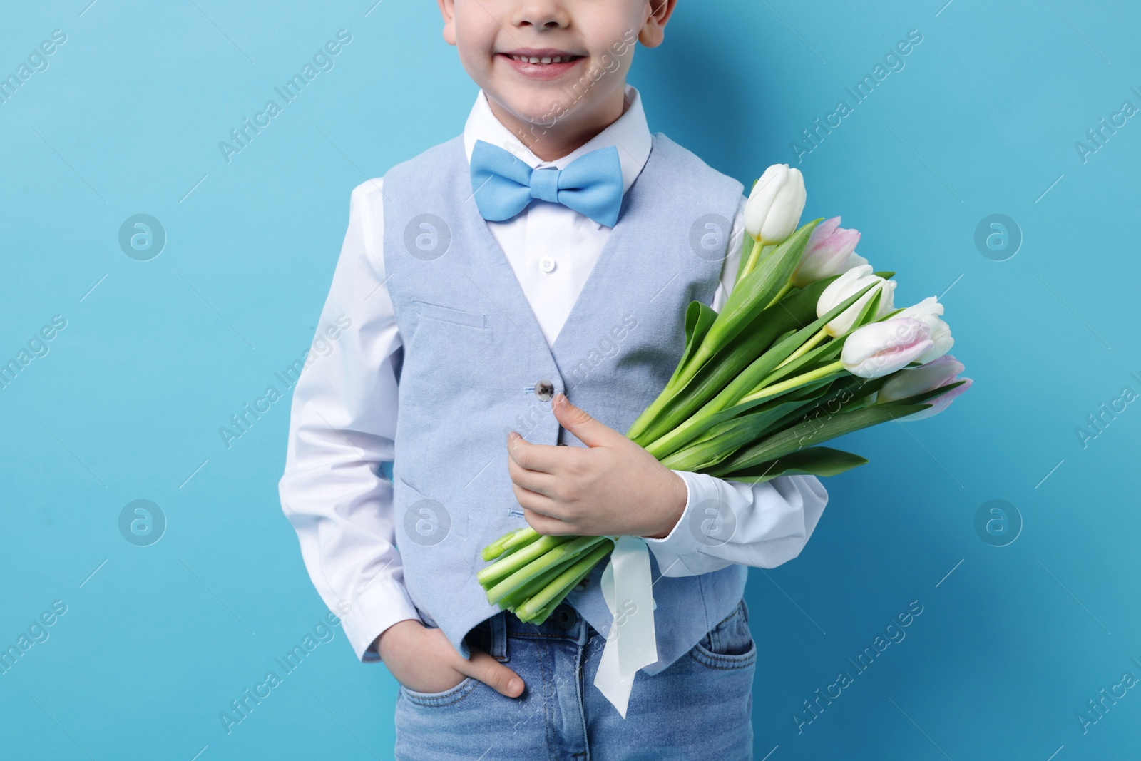 Photo of Little boy with bouquet of tulips on light blue background, closeup