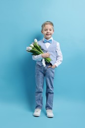 Cute little boy with bouquet of tulips on light blue background