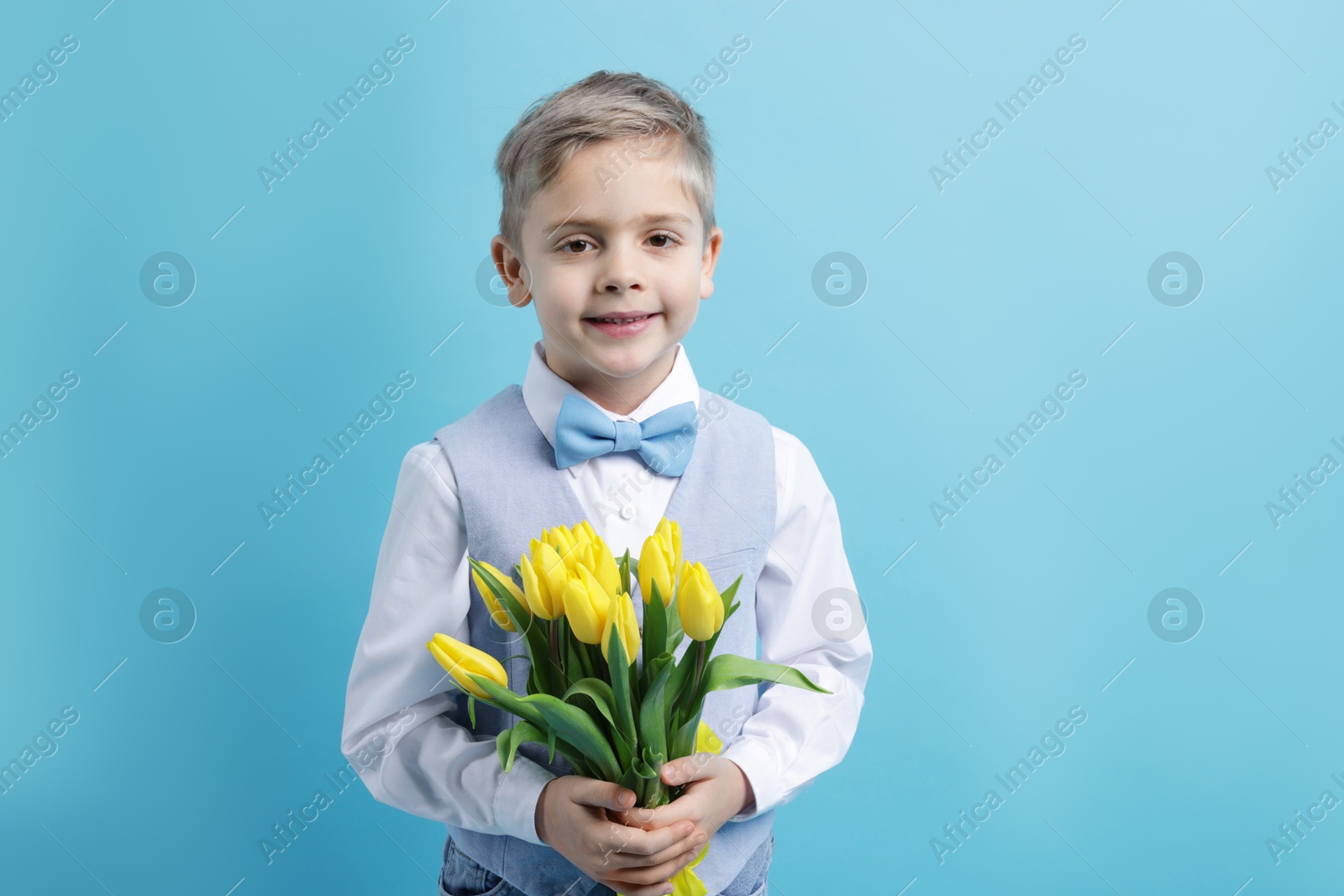 Photo of Cute little boy with bouquet of tulips on light blue background