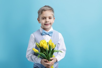 Photo of Cute little boy with bouquet of tulips on light blue background