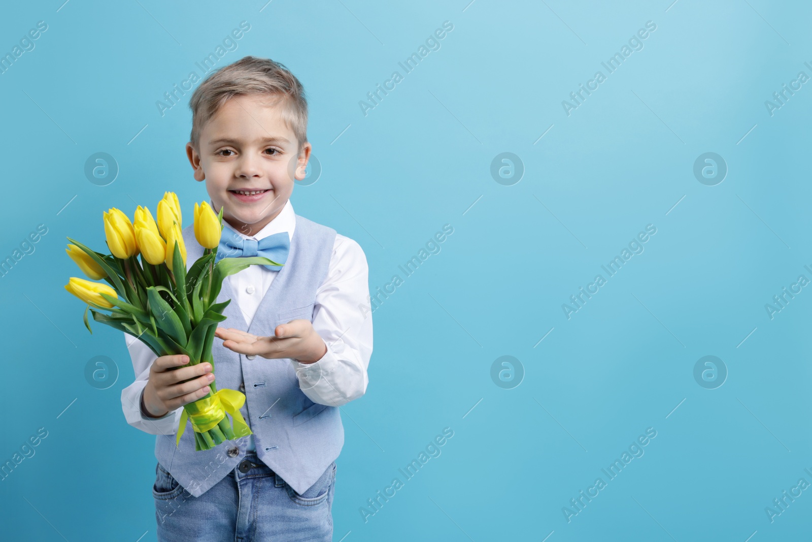 Photo of Cute little boy with bouquet of tulips on light blue background. Space for text