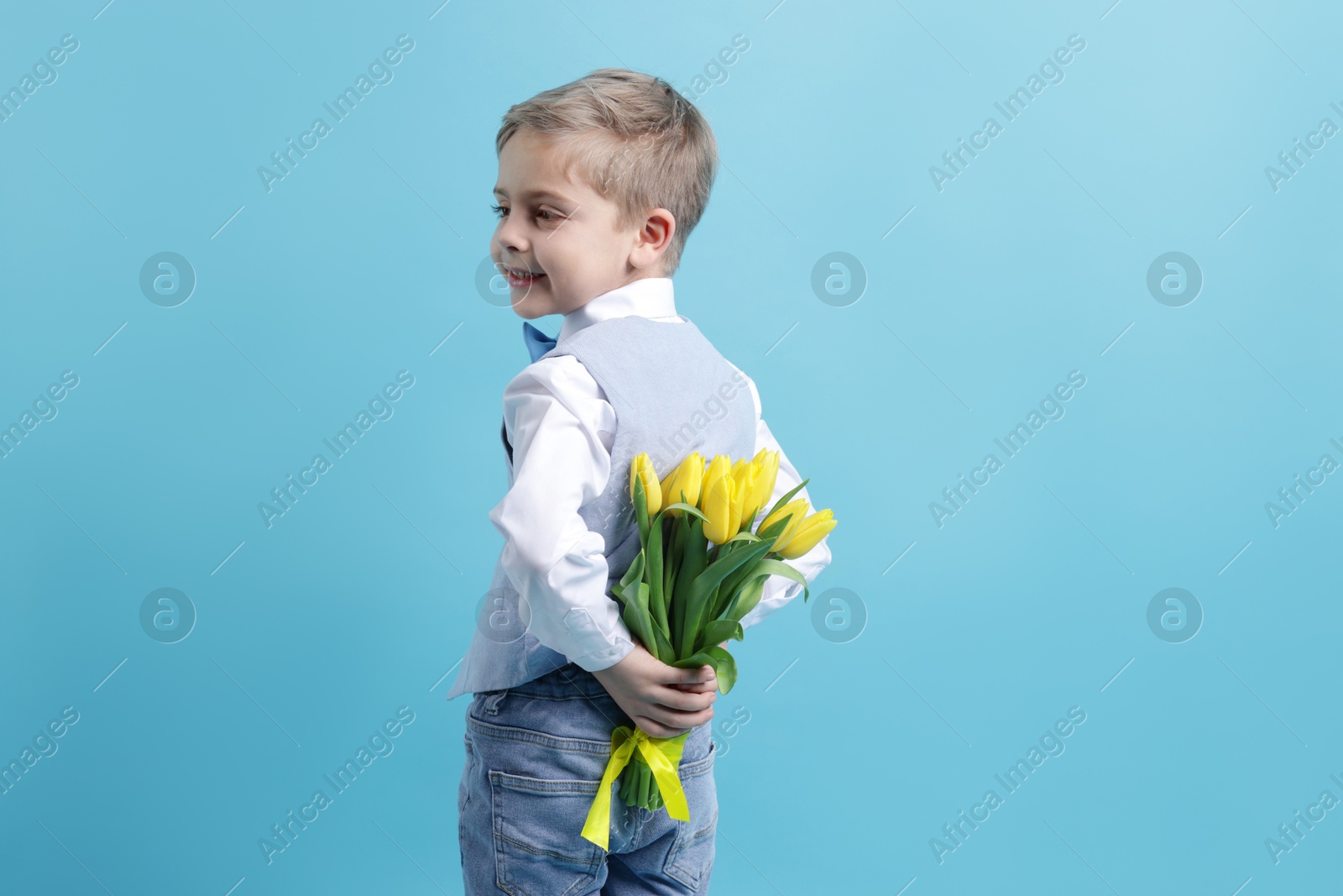 Photo of Cute little boy with bouquet of tulips on light blue background